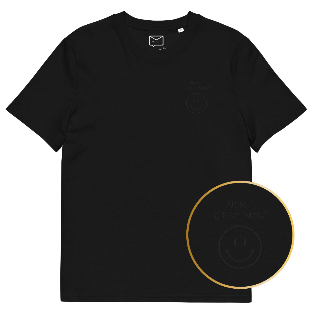 Front view of a black short-sleeved t-shirt featuring a subtle, tonal black graphic on the left side of the chest, consisting of a small smiley face above the French phrase "Noir c'est noir" (Black is black)