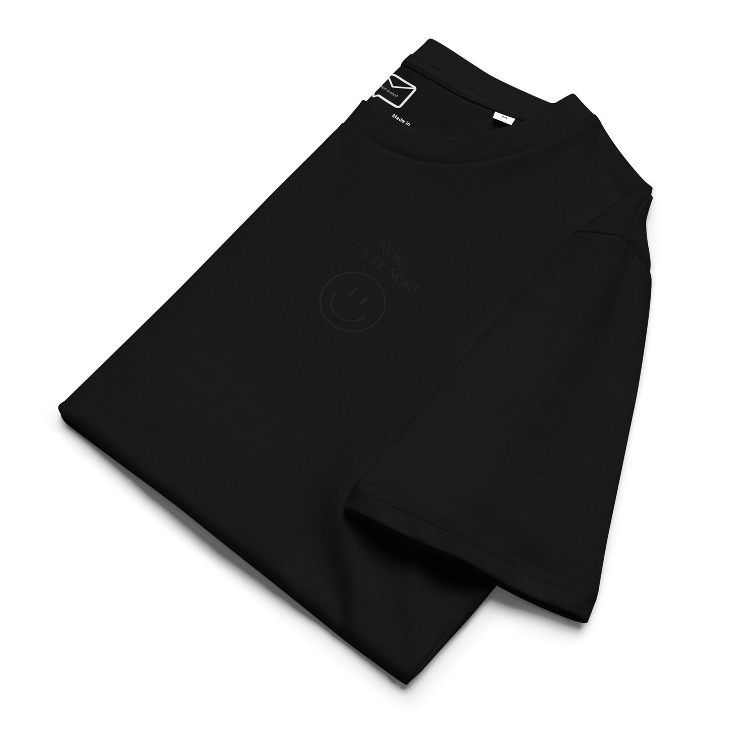Folded view of a black short-sleeved t-shirt featuring a subtle, tonal black graphic on the right side of the chest, consisting of a small smiley face above the French phrase "Noir c'est noir" (Black is black)