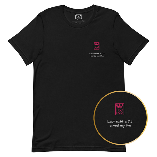 Front view of a black short-sleeved t-shirt featuring a small, illustrated red DJ turntable and the iconic song lyric "Last night a DJ saved my life" in a simple red font beneath it, located on the left side of the chest