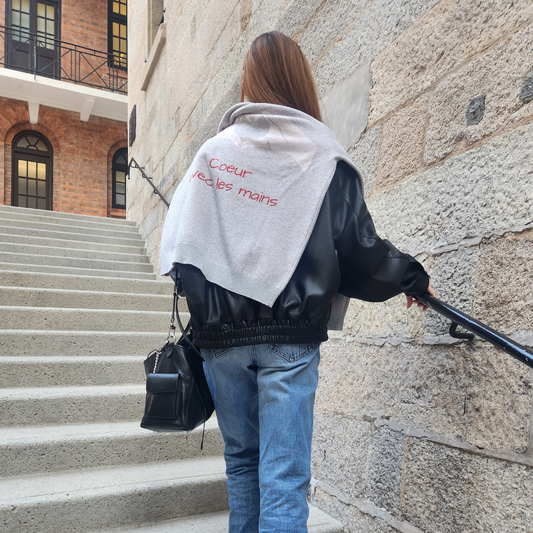 Light grey knitted jumper with a white hand gesture forming a heart and the French phrase "Coeur avec les mains" (Heart with the hands) in red lettering below on the back, and a small embroidered brand tag on the lower right sleeve