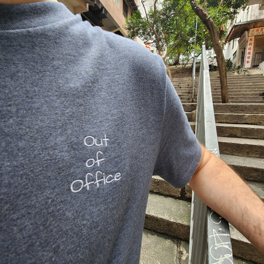 Front view of a grey short-sleeved t-shirt featuring the phrase "Out of Office" in a small, simple white font on the left side of the chest