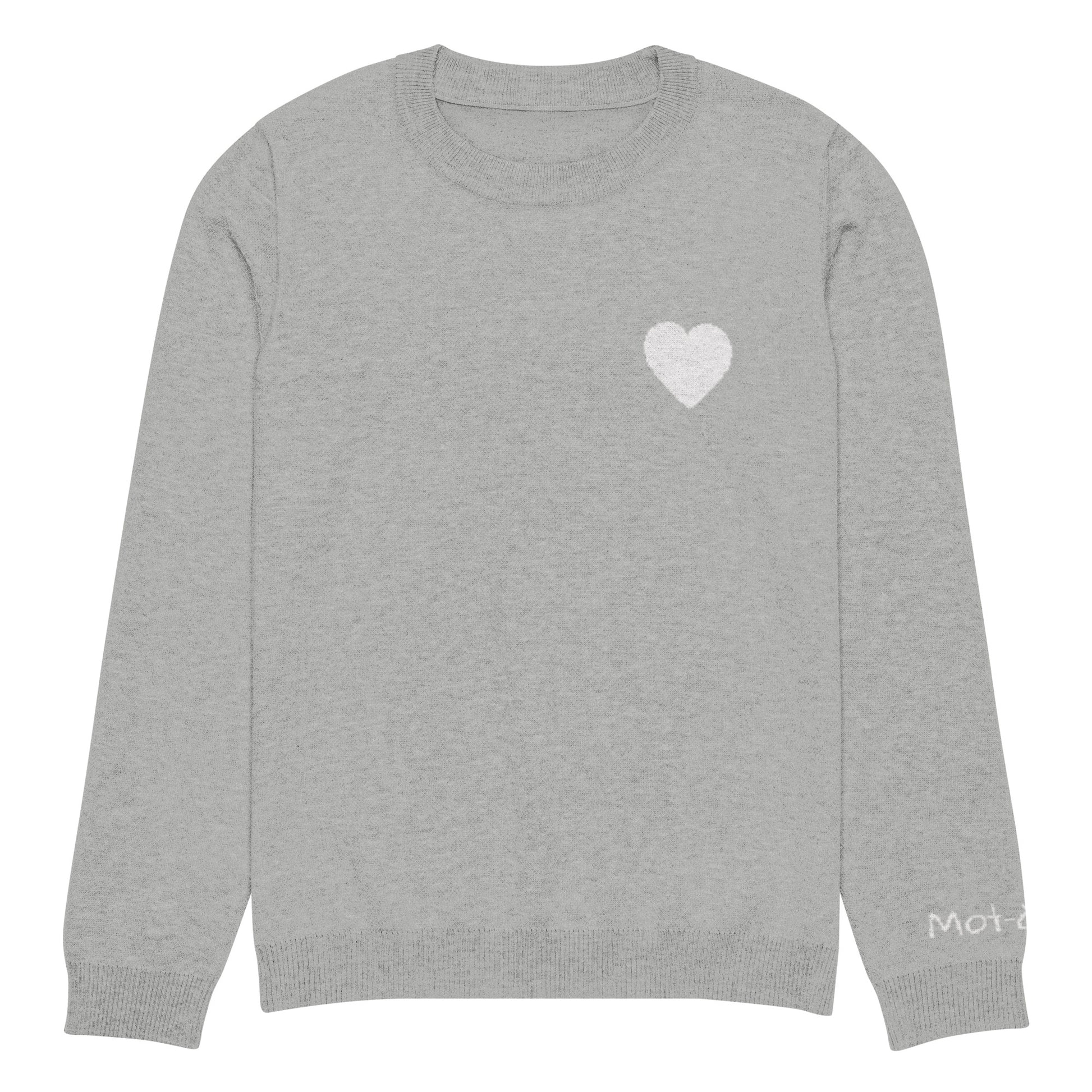 Front view of a light grey knitted jumper with a ribbed neckline, cuffs, and hem. A small white heart design is located on the upper left chest, constructed from the knit itself (jacquard technique). A small embroidered brand tag "mot-à-mot" is visible on the lower left sleeve.