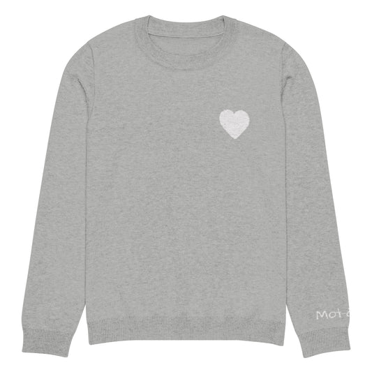 Front view of a light grey knitted jumper with a ribbed neckline, cuffs, and hem. A small white heart design is located on the upper left chest, constructed from the knit itself (jacquard technique). A small embroidered brand tag "mot-à-mot" is visible on the lower left sleeve.